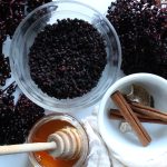 Fresh and dried elderberries with honey comb in a pot full of raw honey cinnamon sticks and dried mushrooms in a white bowl
