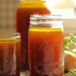 a 1/2 gallon, quart and pint size glass mason jar full of finished instant pot bone broth recipe sitting on counter with fresh onions and herbs sitting next to jars
