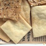 Homemade Sourdough crackers sitting on parchment paper sprinkled with Everything Bagel seasoning and sea salt.