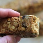 Woman holding a homemade sourdough granola bar with homemade sourdough granola bars in the background sitting on the counter