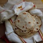 sourdough discard tortillas homemade sitting in cloth on the counter next to a bouquet of flowers