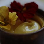 homemade mayonnaise sitting in a pottery bowl with two natsurium flowers sitting atop the mayo
