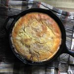 Sourdough Dutch Baby Puff Pancake in a cast iron skillet sitting on a cooling rack on a tea towel on the counter top.