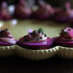 Beet Pickled Eggs sitting on a deviled egg plate garnished with pickled red onions and fresh chives.